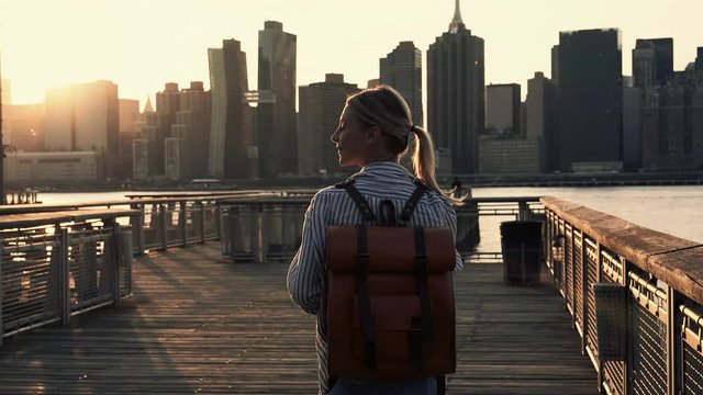 Back view of talented hipster girl using film instant camera for clicking pictures of Manhattan island recreating at Brooklyn side, millennial woman with trendy backpack exploring dream city - New Yor