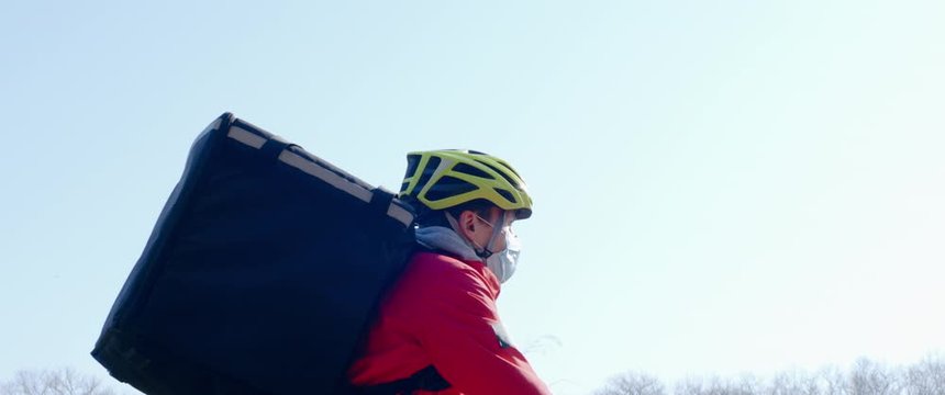 TRACKING CU Courier wearing medical mask and gloves riding a bicycle to deliver food order to customers during virus outbreak. Coronavirus, COVID-19, safe delivery
