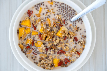 Granola with yellow mango, red goji berries and almond milk, closeup