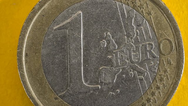 One euro coin rotating on yellow background, stop motion 4k