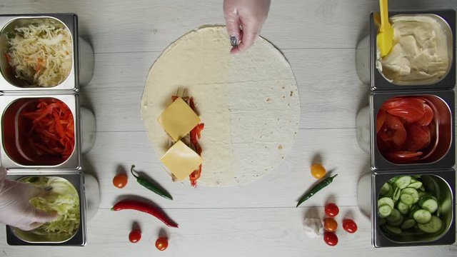 Top view of chef hands in white gloves puts cabbage on doner kebab shawarma in pita or lavash. Shawarma with chicken cutlet, pappers, cheese and vegetable