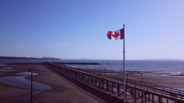 Canadian flag flying in slow motion on a warm, windy, spring day against beach dock.