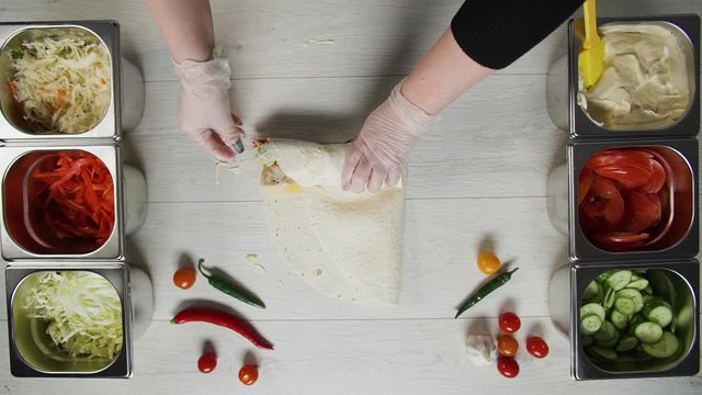 Top view of chef hands in white gloves wraps doner kebab shawarma in pita or lavash. Shawarma with chicken cutlet, pappers, cheese and vegetable