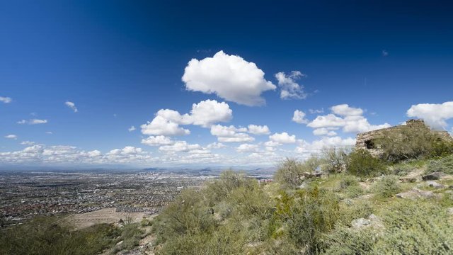 Phoenix, Arizona - March 14 2020: Looking across Phoenix from Dobbins Lookout in a wide timelapse as clouds flow overhead. The lookout building is visible in the foreground.