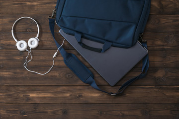 White headphones with a wire and a laptop in a blue bag on a wooden table.