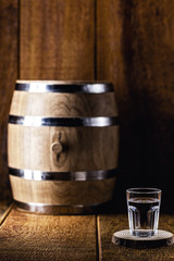 Old oak barrel and glass of high quality distilled alcohol. Brazilian silver cachaça, called pinga, vodka, white rum, liqueur, pure drink, Poitín, sake, brandy or Absinthe.