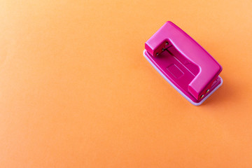 Pink hole punch on an orange background. Close up.