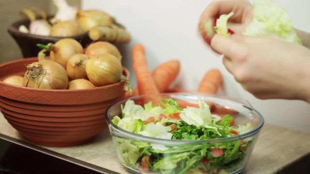 Side-on view of a woman ripping up leaves of lettuce and putting them into a glass bowl to prepare a salad
