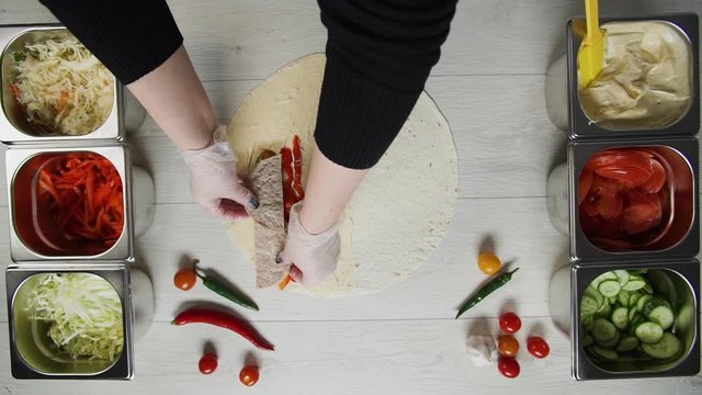 Top view of chef hands in white gloves puts beef cutlet on doner kebab shawarma in pita or lavash. Shawarma with beef cutlet, pappers, cheese and vegetable