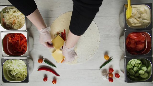 Top view of chef hands in white gloves puts cheese on doner kebab shawarma in pita or lavash. Shawarma with beef cutlet, pappers, cheese and vegetable