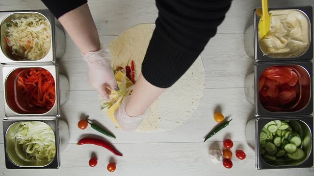 Top view of chef hands in white gloves puts cabbage on doner kebab shawarma in pita or lavash. Shawarma with chicken cutlet, pappers, cheese and vegetable