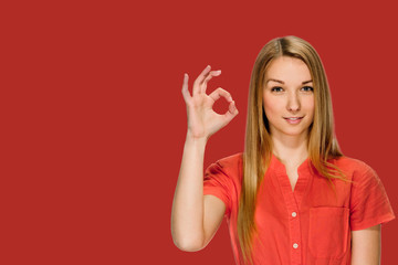 Pretty young blonde gesturing ok on fire brick shade red background