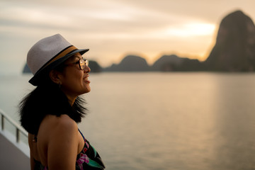 Luxury tourism vacation concept. Selective of focus  happy woman looking at blurry background view of ocean and tropical islands from sailing yacht during golden sunset.