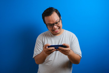 photo of a fat Asian man wearing a gray T-shirt looking happy playing a game on his smartphone