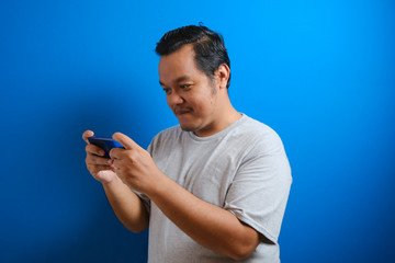 photo of a fat Asian man wearing a gray T-shirt looking happy playing a game on his smartphone