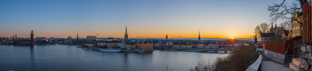 Naklejka na ściany i meble Morning view at sunrise over the districts of old town Gamla stan and the Djurgården with orange skyline with silhouettes a sunny morning in Stockholm from the district of Södermalm.