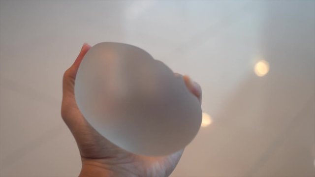 Woman hand holding and squeeze breast implants on white marble background..Softness strength of silicone,used in plastic surgery .