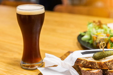 Stout (Black Beer) with froth in a drinking glass on a wooden table with blur food in the background.