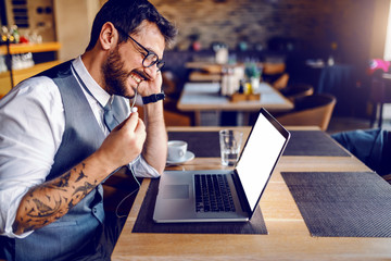 Side view of handsome Caucasian bearded businessman with tattoo and eyeglasses in suit sitting in...