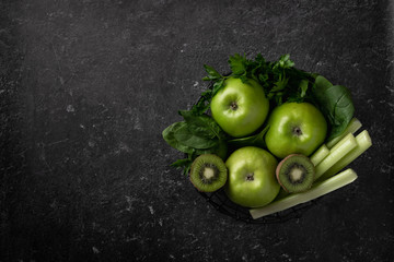 Green fruits and vegetables for making detox smoothie. Apples, kiwi, spinach, celery and parsley on a black background. Top view.