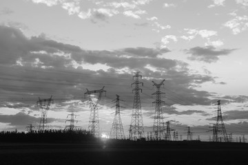 Many high voltage towers, silhouetted against the setting sun