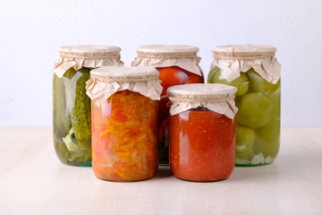 Five jars with preserved homemade cucumbers, tomatoes, lecho, ketchup
