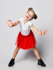 Happy laughing blonde kid girl in red skirt and white t-shirt is bending over with her arms outstretched towards us