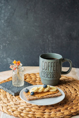 Peanut butter with blueberry, banana and sesame seeds on wholegrain rye crisp bread with mug of hot black coffee on a wooden table