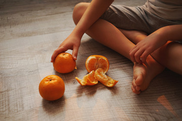 little boy sits on the floor and eats tangerines in a beautiful evening light