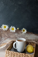White cup of hot herbal chamomile tea with lemon on chamomile grey background