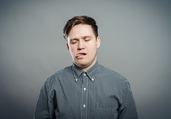 Obraz premium Closeup portrait, funny annoyed young childish rude bully man sticking his tongue out at you camera, isolated gray background. Negative emotion facial expression feelings, signs, symbols