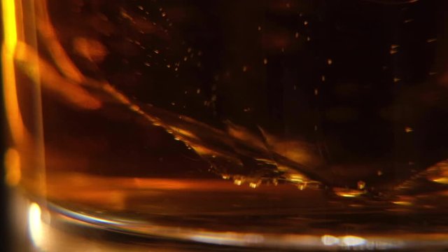Whiskey macro close up of Ice cubes swirling in bottom of glass of whisky or another alcohol in slow motion