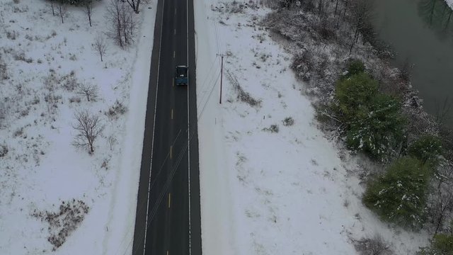 Overhead bird's eye view of blue dump truck driving down highway next to river in winter. Drone aerial, overview. Dolly in