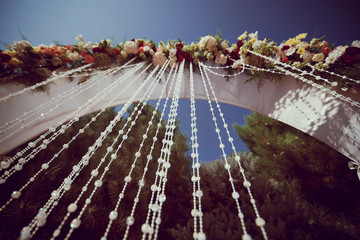 Bright stylish beautiful wedding arch with fresh flowers against the sky
