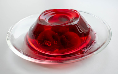 Glass plate with cherry berries in red jelly on a white background.