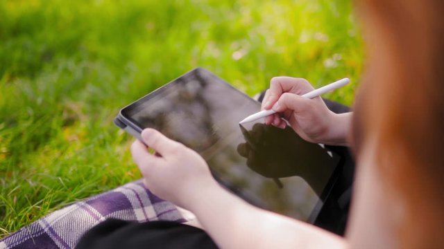 Red haired woman designer drawing on tablet with interactive Pen