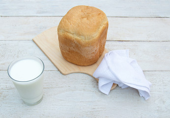 Fresh homemade bread and a glass of natural homemade organic yogurt on a white wooden background.