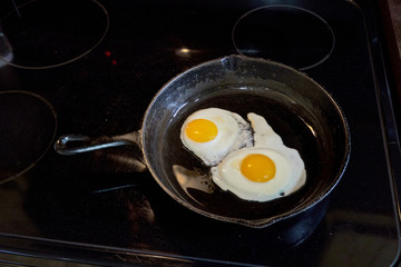 Breakfast Two sunny side up eggs fsliding out of a cast iron skillet on white plate