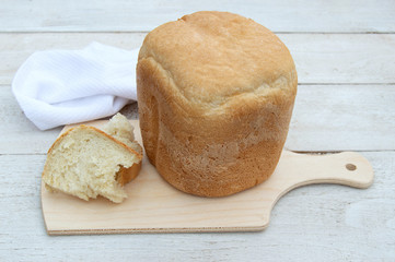 A loaf of fresh homemade bread on a wooden board on a white wooden background. The view from the top.