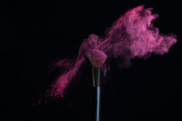 Make-up brush with pink powder explosion isolated on a black background