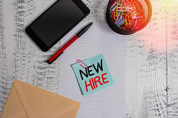 Handwriting text New Hire. Conceptual photo someone who has not previously been employed by the organization Smartphone paper sheet clips holder pen envelope note wooden background