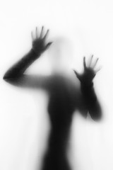 Concept of a frightened woman behind sheet with backlighting in monochrome - 339815310