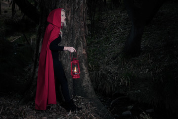 Attractive woman dressed a little red riding-hood walk in a dark forest with lantern