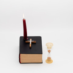 An hourglass, a burning candle and a cross on the Bible, symbolizing the times of the end of the world according to the Holy Bible. Time is running out.