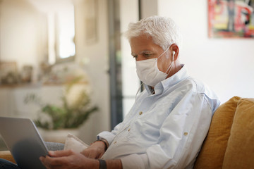 Man at home working on laptop, wearing face mask during pandemic