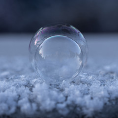 Zwei schillernde gefrorene Seifenblasen hintereinander auf Schnee