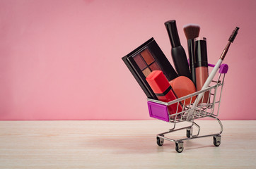 Shopping trolley full of make up and cosmetic goods on pink background. Black friday concept. Sale and discount. Goods for women. Closeup of a basket with products for make-up. 