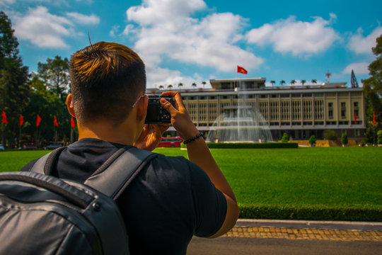 Back side of Young Asian traveling men taking a photo of Independence Palace in Ho Chi Minh City, Vietnam.  Independence Palace is known as Reunification Palace and was built in 1962-1966. 