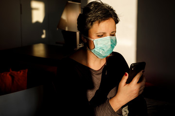 Donna Bianca con i capelli scuri indossa un mascherina chirurgica e osserva il suo smartphone