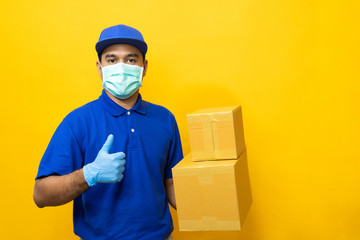 Obraz na płótnie Canvas Delivery man blue uniform wearing rubber gloves and mask holding parcel cardboard box on yellow background.